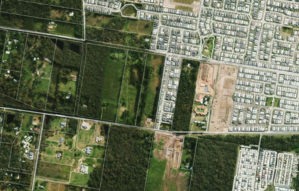 Aerial view of a greenfield site with land cleared for residential subdivision, surrounded by bushland and road frontage, representing the Park Ridge Logan development.
